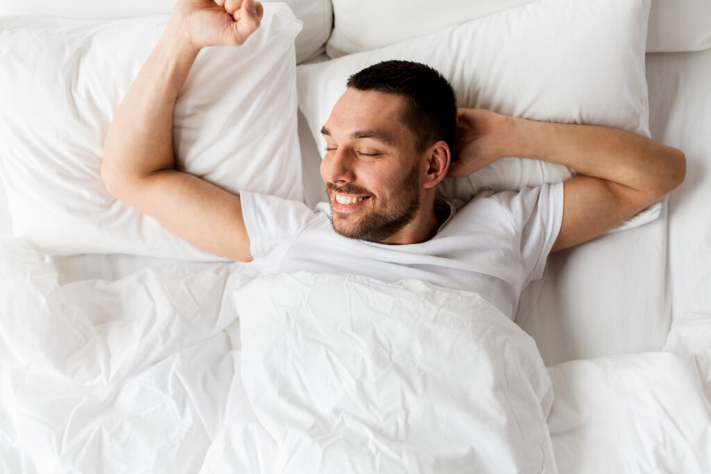 Man waking up in bed happy after a good night's sleep.