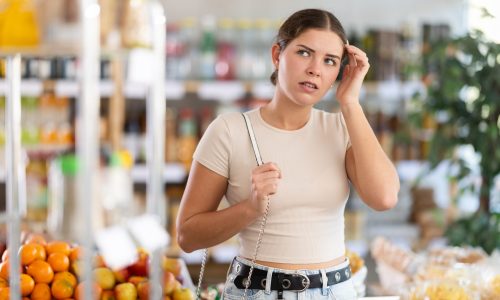 Young woman buyer forgot what she wanted to buy woman in the middle of the grocery store forgetting what she is supposed to get.