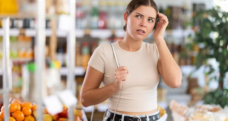 Young woman buyer forgot what she wanted to buy woman in the middle of the grocery store forgetting what she is supposed to get.