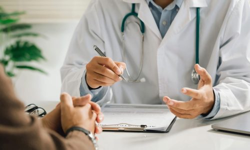A professional physician in a white medical uniform talks to dis A professional physician in a white medical uniform talks to discuss results or symptoms and gives a recommendation to a male patient and signs a medical paper at an appointment visit in the clinic.
