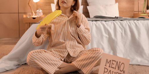 Mature woman with fan suffering from hot flashes in bedroom at night. Menopause concept Mature woman with fan suffering from hot flashes in bedroom at night. Menopause concept