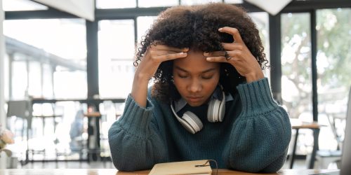 Tired Young Woman Studying Online with Headphones in Modern Home, Looking Stressed and Overwhelmed A young woman with headphones, looking tired and stressed while studying online in a modern home setting.