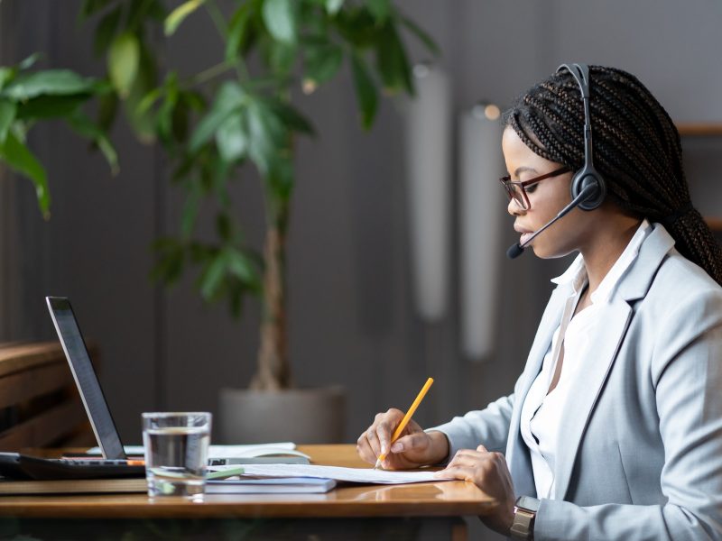 focused-african-female-home-based-virtual-assistant-in-headset-making-notes-during-online-meeting.jpg